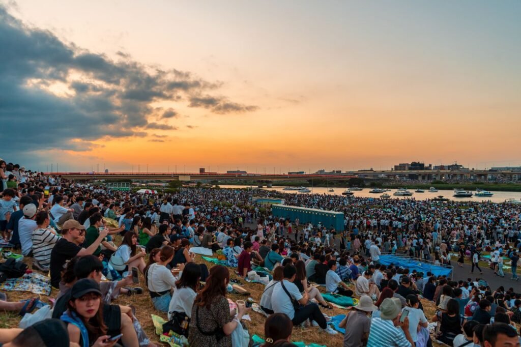 A vast crowd enjoys a festival by the river in Tokyo, Japan, during sunset.